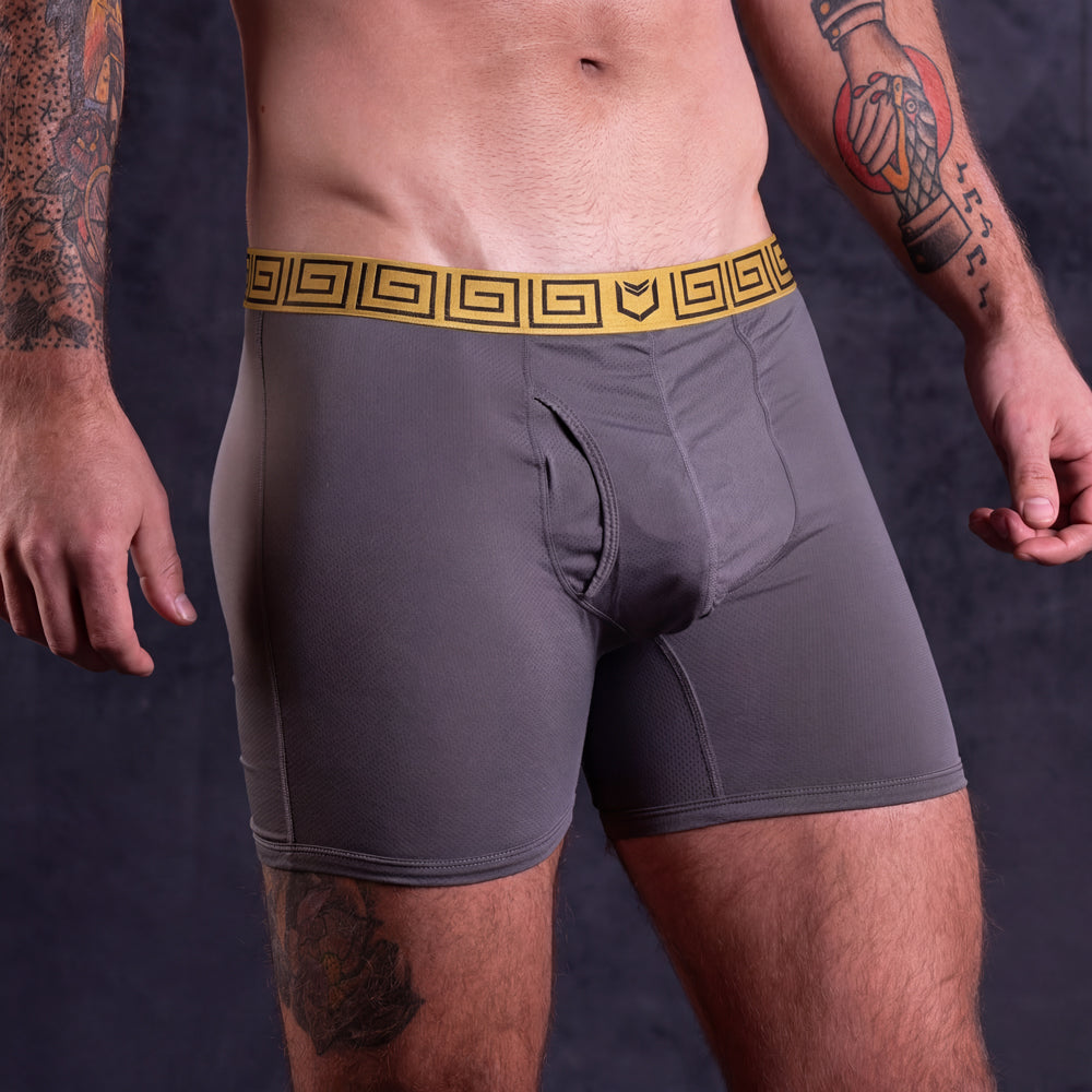Man wearing SHEATH AirFlow gray mesh boxer briefs with a gold waistband on a dark background