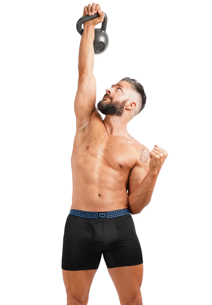Man lifting a kettlebell above his head wearing SHEATH AirFlow black boxer briefs with a blue waistband on a white background