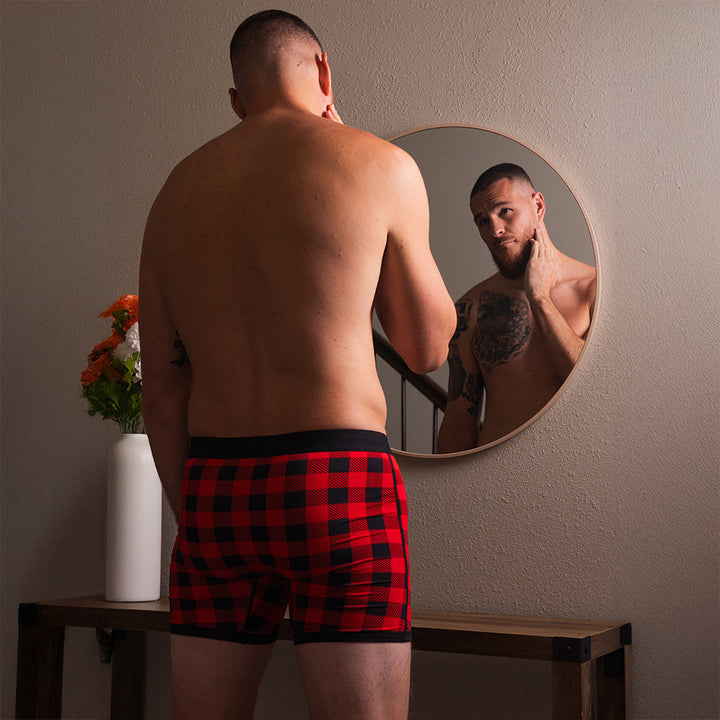 Man in red and black holiday plaid dual pouch boxer briefs looking at himself in a mirror.