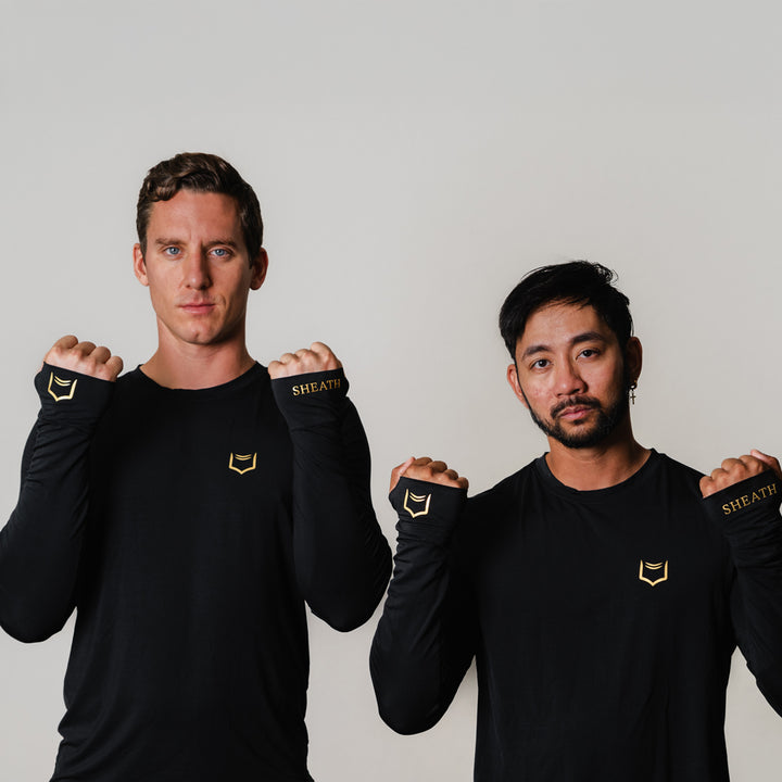 Two models wearing SHEATH Baselayer Top With Golden Heat Print Logo On Lapel and Cuffs - Black