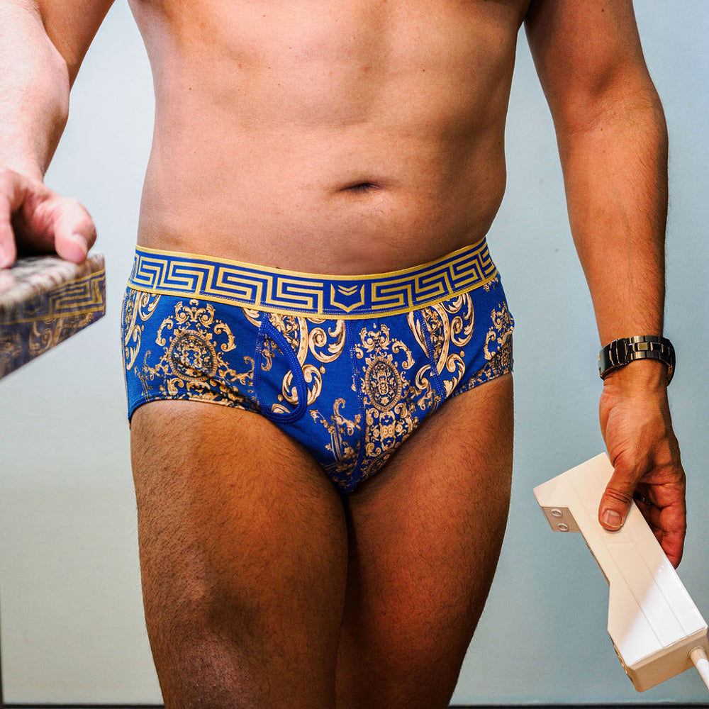Male model holding old-fashioned cellular phone and wearing SHEATH scepter blue ornamental pattern american cut brief with dual pouch ergonomic support, made from breathable modal fabric featuring moisture-wicking and anti-chafing properties for all-day comfort.#color_scepter-blue