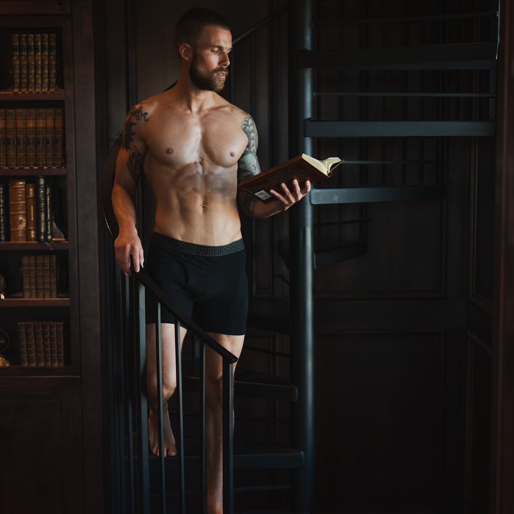Male model reading a book while wearing SHEATH black boxer briefs made from breathable bamboo airflow mesh fabric with ergonomic dual pouch support for anti-chafing comfort and everyday wear