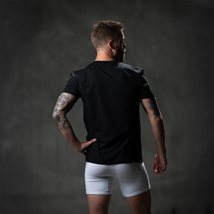 Male model wearing SHEATH black t-shirt featuring breathable bamboo fabric and a crew neck, with a black logo on the breast for athletic and casual wear. back view