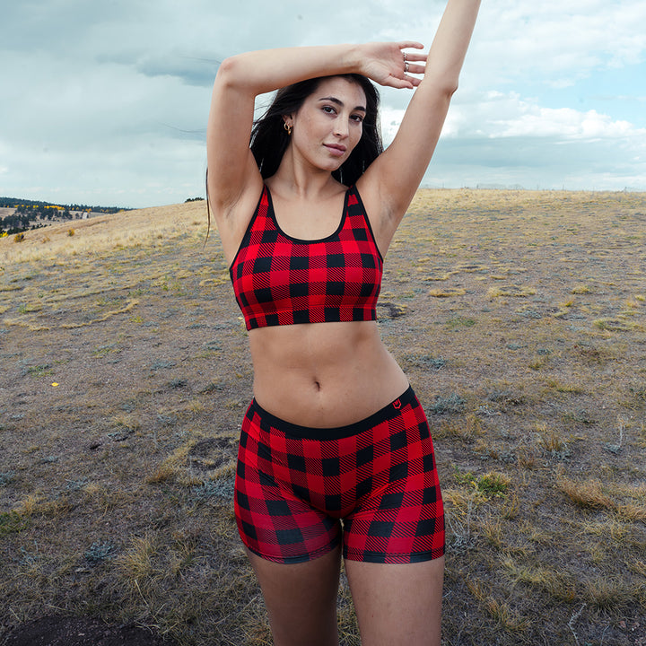 Woman wearing a red and black holiday plaid boxer briefs with matching bralette in an open field.