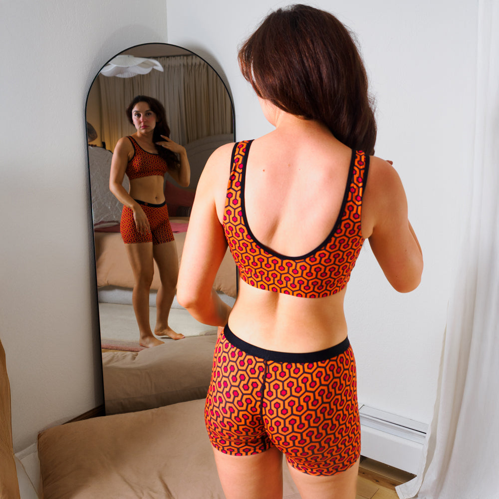 Woman wearing women's boxer brief - orange hexagon pattern with matching bralette standing in front of a mirror.